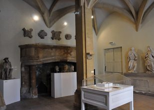 Salle médiévale réaménagée avec cheminée et statues.