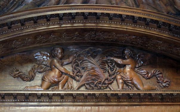 Dans le tympan du banc d'œuvre, deux anges entourent une couronne qui reçoit deux palmes de martyre