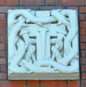 Bas–relief sur la façade : le Tau est un symbole de la Croix.